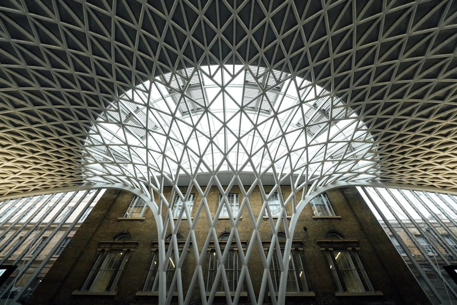 An expansive view of King's Cross railway station interior during evening hours, showing multiple platforms with trains parked along the tracks. The station features a high, arched ceiling constructed