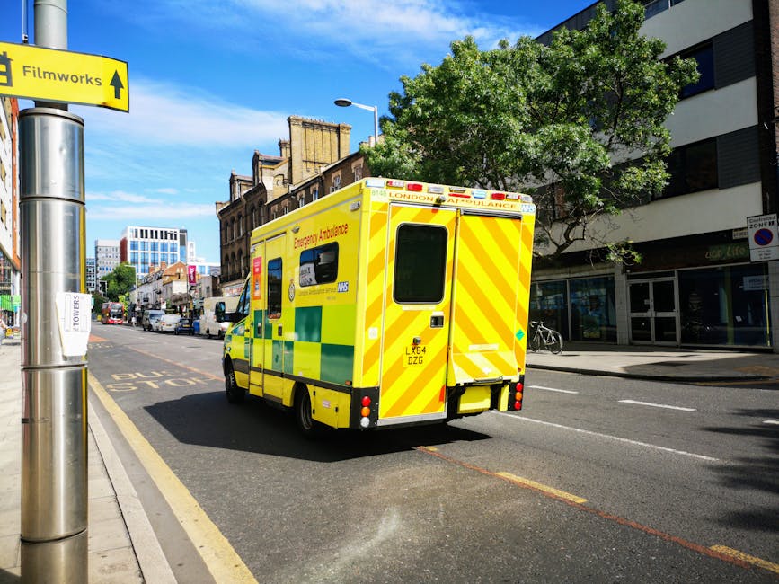 A white waste collection truck with signs of rust and wear on its rear compactor, is parked on a cobblestone street alongside a row of older multi-storey buildings. A worker dressed in blue overalls a