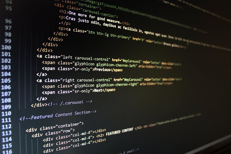 Close-up of a person's hands typing on a laptop with a dark-themed code editor open, displaying lines of code in various colors such as green, blue, and white. The laptop is positioned on a black desk